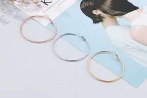 Detailed view of large twisted metal hoop earrings in gold, silver, and rose gold