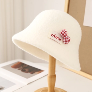White lamb wool bucket hat with red plaid bow decoration on wooden stand