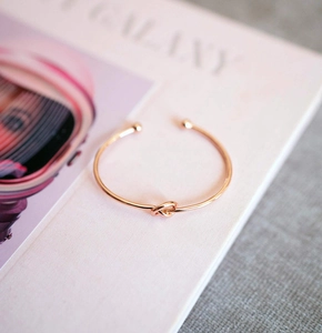 Detail of rose gold knot cuff bangle on magazine, showing minimalist open bracelet design