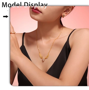 Close-up of golden angel wing heart necklace worn by a model on a soft pink background