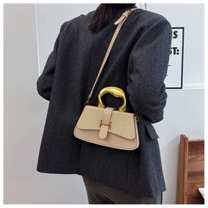 Close-up of beige leather crossbody bag with woven flap and stylish gold metal handle