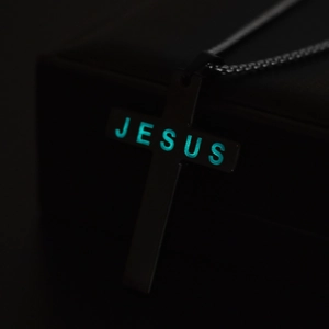 Vue macro du collier croix Jésus lumineux brillant en bleu sur fond noir profond