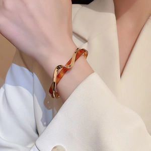 Detail of cross-layered wavy gold cuff bracelet with amber resin insert on model wrist