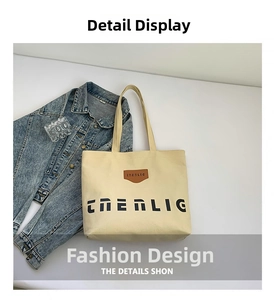 Detail of beige canvas tote bag with black lettering and brown leather brand label