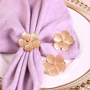 Close-up of three gold metal flower napkin rings set on white cloth and ceramic plates