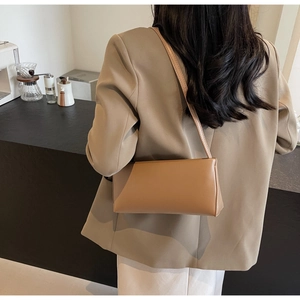 Rear view of a model wearing the brown leather underarm bag with a minimalist design