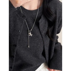 Silver Y-necklace with horse pendant and bell charm worn on a dark grey sweater