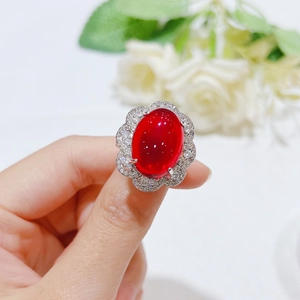 Macro shot of a red ruby oval ring with a floral zircon halo worn on a hand