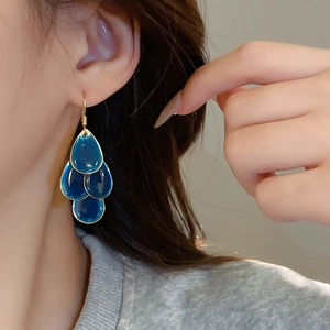Detail of layered blue teardrop earrings featuring golden edges and refined resin gems