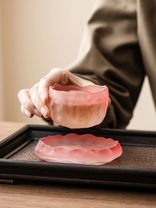 Close-up of pink frosted glass teacup and saucer with elegant wavy edges on a wooden tray