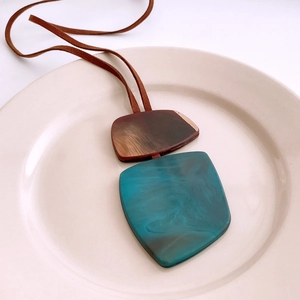 Detail shot of the teal resin and wood grain pendant on a long brown suede necklace