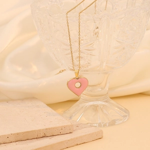 Détail d'un pendentif cœur en émail rose sur une fine chaîne dorée avec un fond en soie
