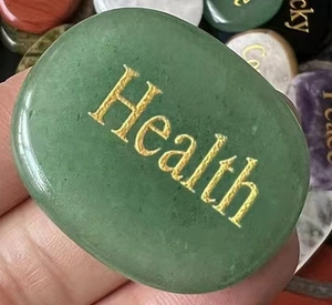 Close-up of green natural stone with gold Health engraving being held in a hand