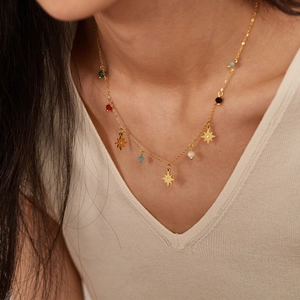 Detail of gold star pendant necklace with colorful beads worn on white knitwear