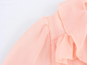 Detail of pink chiffon dress showing ruffled shoulder design and V-neckline texture