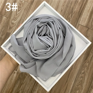 Détail d'un foulard en mousseline gris foncé avec paillettes dorées plié en rose