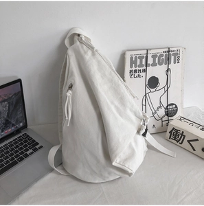 Detail of a minimalist white canvas crossbody bag with adjustable strap on a desk