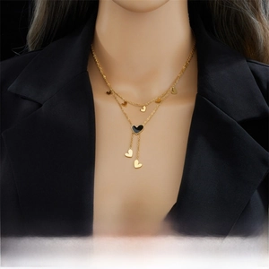 Detail of layered gold titanium necklace with black heart enamel and heart tassel