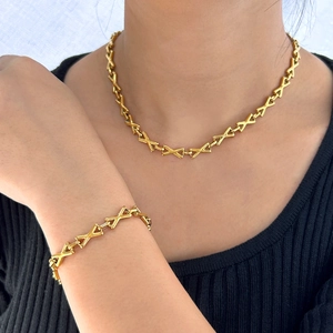 Golden necklace and bracelet set featuring X-shaped geometric links on a fashion model