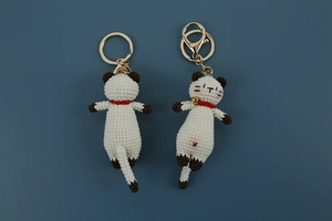 Front and back detail of hand-knitted white cat keychains with red collars and bells