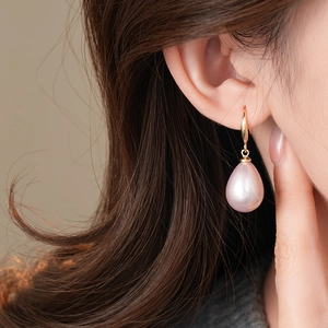 Close-up of elegant gold hoop earrings with pink teardrop pearls on a model