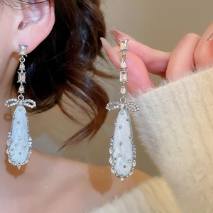 Detail of silver bow earrings with zircon stones and shimmering teardrop pendant drops