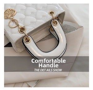 Close-up detail of a white heart-quilted handbag with gold heart charm and thick handle