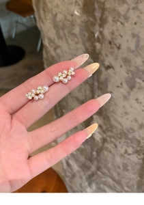 Detail of gold-plated flower pearl earrings with green zircons held in a lifestyle setting
