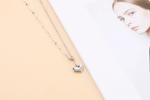 Detailed view of silver heart pendant with fine beaded chain on a minimalist background