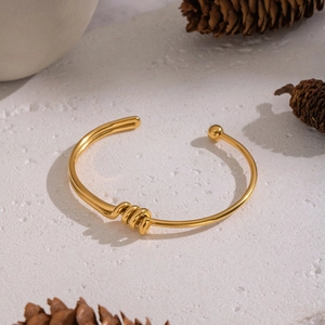 Detailed view of gold knot bangle with ball end on white textured stone with pine cones