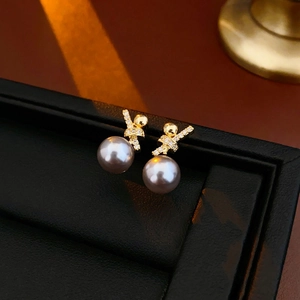 Macro shot of 18k gold plated pearl earrings with zircon inlay on luxury black leather