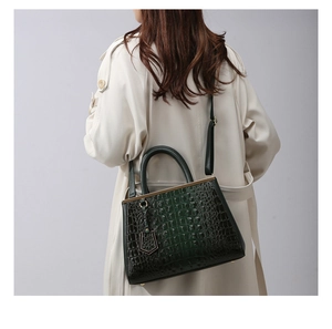 Detail of dark green crocodile texture handbag with gold hardware on a model
