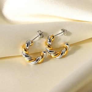 Detailed view of two-tone twisted C-shape earrings on soft beige silk fabric background