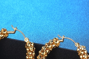 Macro shot of gold hoop earrings with intricate beaded texture on a blue surface