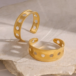 Detail view of two gold chunky hollow cuffs with rope texture on a stone background