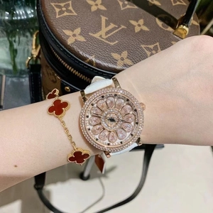 Detail of luxury rose gold watch with rotating floral dial and red clover bracelet