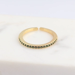 Detail of a golden adjustable ring with micro-set green zircons on a marble surface