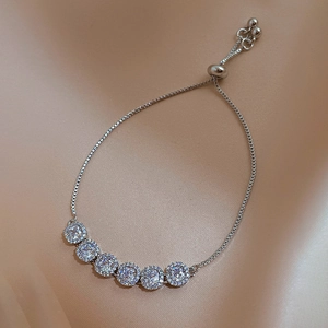 Detail of adjustable silver bracelet with six halo-set cubic zirconia stones on silk fabric