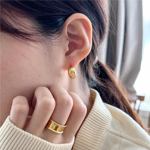 Close-up of minimalist gold matte hoop earrings and wide ring on a model in knitwear