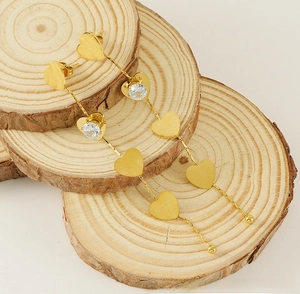 Detail of long gold heart tassel earrings with zircon stones on natural wood slices