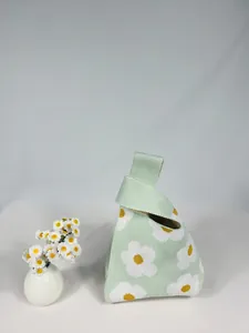 Detail of light green knitted bucket bag featuring white daisy patterns and handle texture