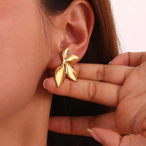 Close-up of a model wearing large golden leaf-shaped textured earrings in a C-shape design