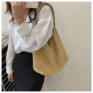 Hollow weave straw shoulder bag shown on model with reinforced straps and soft mesh texture