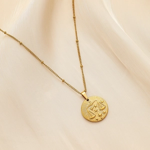 Detail of Libra constellation pendant on beaded gold chain over beige silk fabric