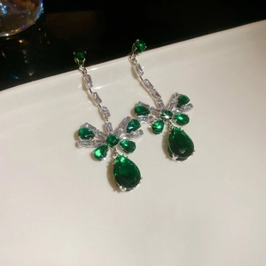 Detail of silver bow earrings with green teardrop zircon crystals on white tray