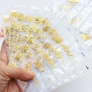 Golden and silver metal nail art charms in various shapes displayed in clear plastic trays