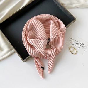 Detail of pink pleated silk scarf neatly arranged on a minimalist black tray with a card