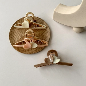 Three acrylic heart-shaped hair claws in beige, pink, and brown on a wood coaster