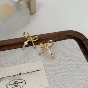 Detail of elegant gold bow earrings with white pearls displayed on a wooden jewelry tray