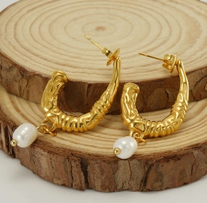 Close-up of gold U-shaped earrings with irregular texture and baroque pearls on wood